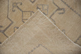 Distressed beige Oushak runner pile with faint grey geometric motifs and woven foundation.