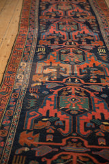 Down-the-length perspective of a vintage Malayer runner with rust and blue geometric figures on a navy field.