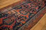 Angled view of a vintage Persian Malayer runner's rust floral border and navy geometric field.