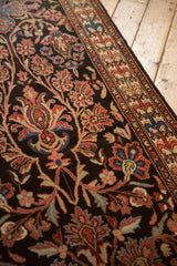 Angled detail of scrolled vines and floral motifs on the dark charcoal field of a vintage Malayer runner.