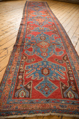 Angled perspective of an antique Heriz runner showing repeating blue turtle medallions on a red field.