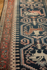 Angled view of a Malayer runner's pictorial hunting scene, dark teal pile, and detailed vine border.