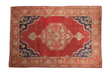 Vintage Oushak carpet, a central floral medallion on abrashed red ground with blue corner spandrels.