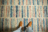 Long shaggy pile of a Moroccan design carpet with abstract stripes in ivory, blue, and blush.