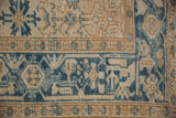 Distressed vintage Mehrivan rug close-up: worn blue geometric guls, meandering border.