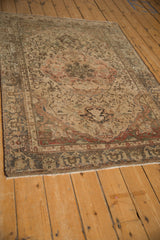 Angled view of a distressed Malayer rug showing even wear across its terracotta and ivory floral designs.