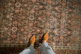 Close view of the distressed Tabriz rug's texture, highlighting the red and charcoal Herati design.