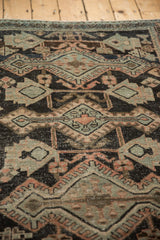 Distressed texture of a vintage Hamadan rug, showcasing geometric charcoal, melon, and silver patterns.