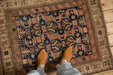Distressed navy blue and dusty blush Caucasian rug featuring geometric motifs and starburst border.