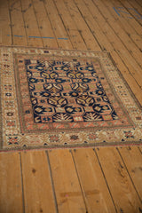 Distressed antique Caucasian rug's starburst border, navy field, and germinating plant pattern.