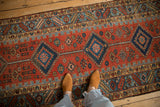 A person's view standing on an antique Persian runner with red and blue geometric medallions.
