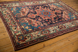 Angled view of a vintage Persian Bakhtiari rug with intricate floral patterns in navy, red, and blush.