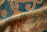 Textural fold of antique Chinese rug, highlighting time-softened dusty blue and beige scrolling vines.