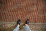 Distressed vintage Mir Sarouk rug with brick red field, repeating boteh pattern, worn texture.