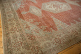 Angled view of a distressed Persian rug's corner, with a detailed sea foam border and worn brick red field.
