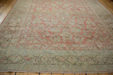 Angled view of a distressed Sarouk carpet's faded grapefruit field and intricate sand-colored border.