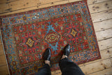 Geometric Karaja rug with brick red field, sky blue medallions, and a Samovar border, shown with feet.