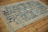 Distressed Hamadan rug corner, displaying worn pinwheel floral border and muted navy diamond patterns.