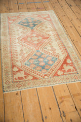 Angled view of a distressed Shiraz rug with ruby red and sky blue medallions and animals in the corners.