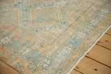 Distressed Afshar rug corner featuring faded blue and orange geometric patterns, plus fringe.