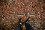 Standing view showing the distressed texture of a vintage Heriz rug in madder red and charcoal.