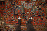 Vintage Heriz carpet with geometric motifs, rich brick red, navy blue, and sneakers.