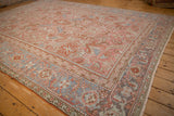 Angled perspective of a distressed Heriz rug highlighting its blush floral field and slate blue border.