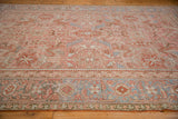 Surface view of a distressed Heriz carpet with a decorative blue Herati border and pale blush field.