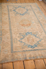 Angled view of a distressed Malayer rug's soft ivory field and blue geometric medallions.