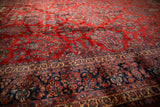 Angled view of a vintage Kazvin carpet showing texture and depth in its red and navy pile.