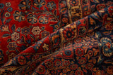 A fold in the vintage Kazvin carpet reveals its plush pile and floral motifs in cherry red and navy blue.