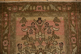 Close-up of a distressed Bibikabad rug's coffee brown vine border and pale pink floral field.