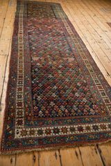 Angled view of a vintage Kurdish Hamadan runner with a colorful repeating blossom pattern.