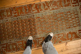 Repeating boteh pattern and worn texture on a distressed terracotta Hamadan runner.