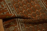 Textured, low pile of a folded antique Hamadan rug showing staggered boteh patterns in rust and ivory.
