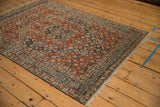 Vintage Persian Bijar rug with a rust red Herati pattern shown from a side angle on a wood floor.