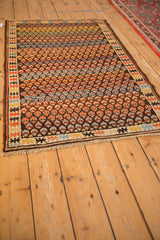 Antique Caucasian rug detail showing geometric border and rainbow-colored germinating blossoms.
