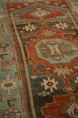 Angled view of the distressed Malayer rug's low pile and geometric motifs in rust and powder blue.