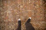 Distressed vintage Malayer carpet with scrolling botanicals, muted golds, and wide floral border.