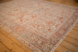 Angled view of a distressed Heriz rug with geometric floral patterns and a detailed dusty blue border.