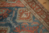 Angled view of a distressed Hamadan rug corner in red and blue with geometric ram's horn motifs.