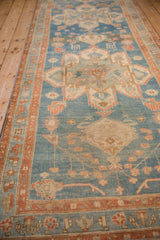 Angled perspective down a distressed Persian runner showing heavy abrashes across its geometric blue and terracotta pattern.
