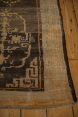 A corner view of the antique Tibetan rug showing its geometric border and low-pile texture.