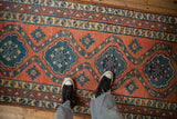 A scale view of the antique Persian runner's brick red ground with dusty teal geometric medallions.