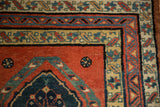 Intricate floral and geometric borders in dusty teal, navy, and saffron on a brick red field.