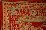 Detailed corner of a vintage Oushak rug with saffron and sky blue hook and latch borders on a cherry red field.