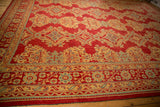 Angled view of the vintage Oushak carpet's geometric border in saffron yellow and sky blue on a red field.