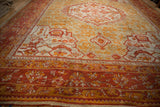 Antique Oushak carpet's madder red border, saffron floral patterns, and seafoam green field.