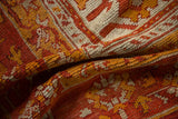 Draped close-up of antique Oushak rug pile with madder root red, saffron, and ivory floral motifs.