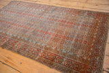 Angled detail of the Distressed Belouch rug, showing repeating floral motifs and geometric borders in dusty blue and chestnut tones.